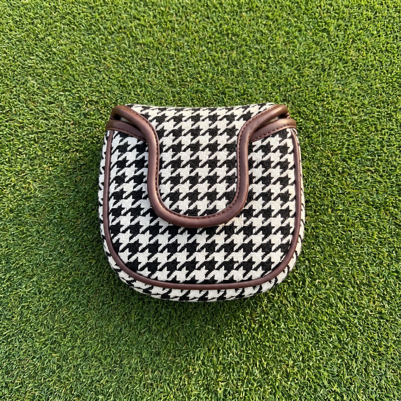 Houndstooth mallet putter cover with brown leather trim, flat lay on golf green